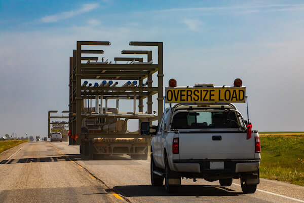 Pilot car escort pickup with OVERSIZE LOAD sign trailing a wide load
