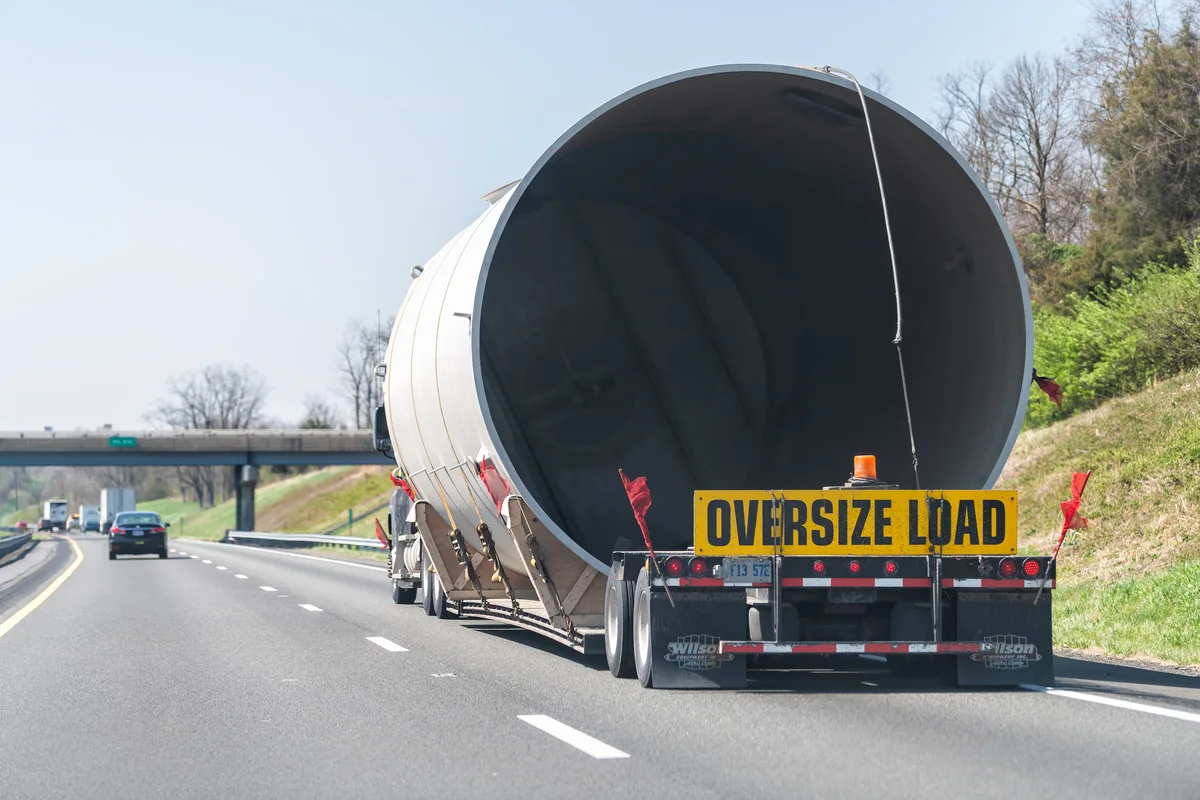Oversize load — large pipe section being hauled on a flatbed trailer with OVERSIZE LOAD banner